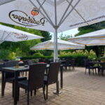 Bestuhlte Restaurantterrasse mit Sonnenschirmen und Sitzplätzen im Grünen.