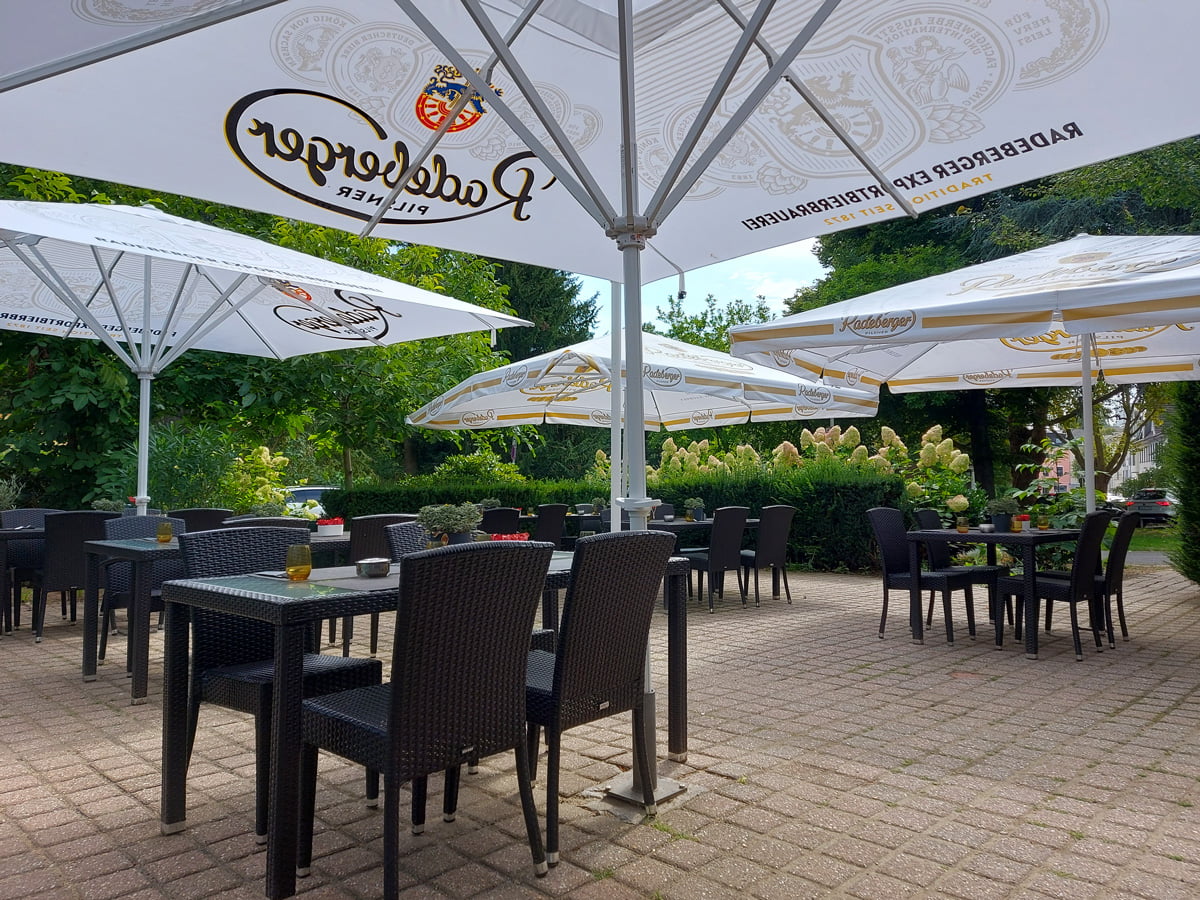 Bestuhlte Restaurantterrasse mit Sonnenschirmen und Sitzplätzen im Grünen.